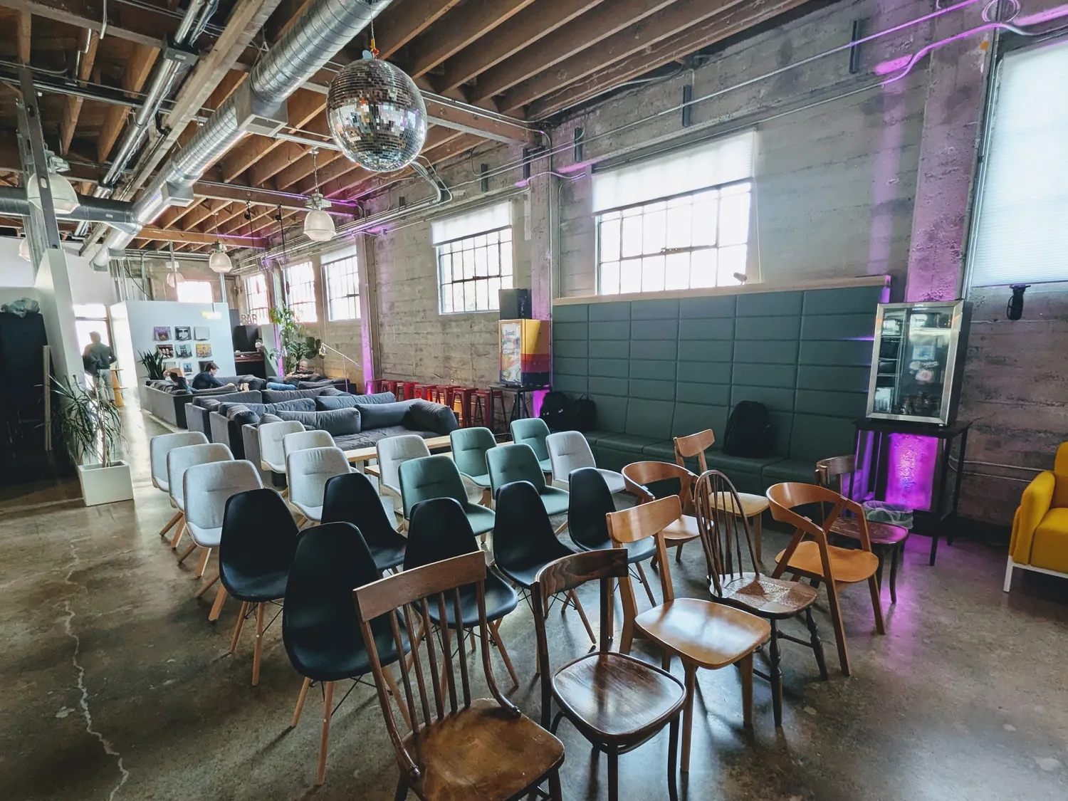 Rows of mismatched chairs set up theater-style in the main House of AI room, under exposed beams and a disco ball
